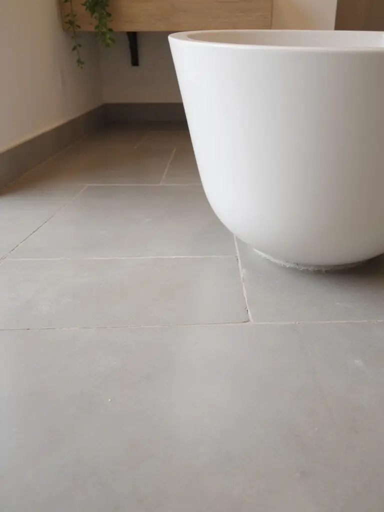 Modern bathroom with warm, light grey heated tile floor and a sleek bathtub.